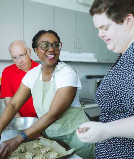 Three people standing in a kitchen baking cookies.